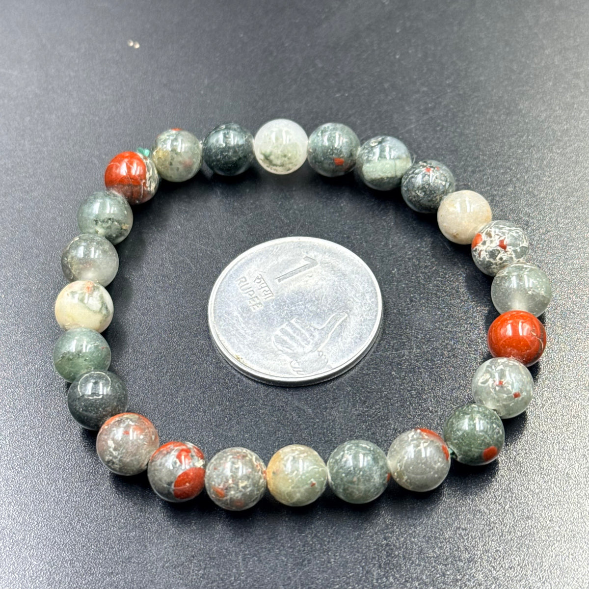 Conglomerate jasper bracelet close-up showing rounded green and orange beads with coin for scale