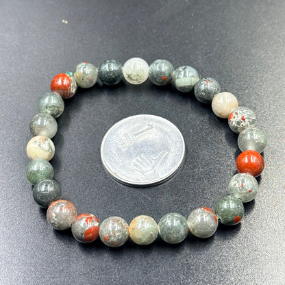 Conglomerate jasper bracelet close-up showing rounded green and orange beads with coin for scale