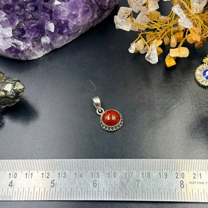 Carnelian 925 silver locket pendant with red oval gemstone, shown on black surface with ruler
