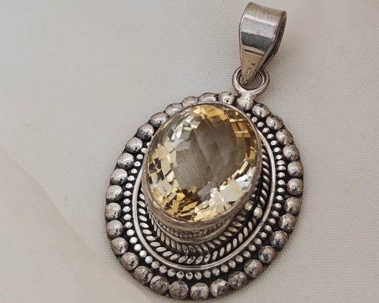 Silver pendant with a yellow gemstone on a light gray background