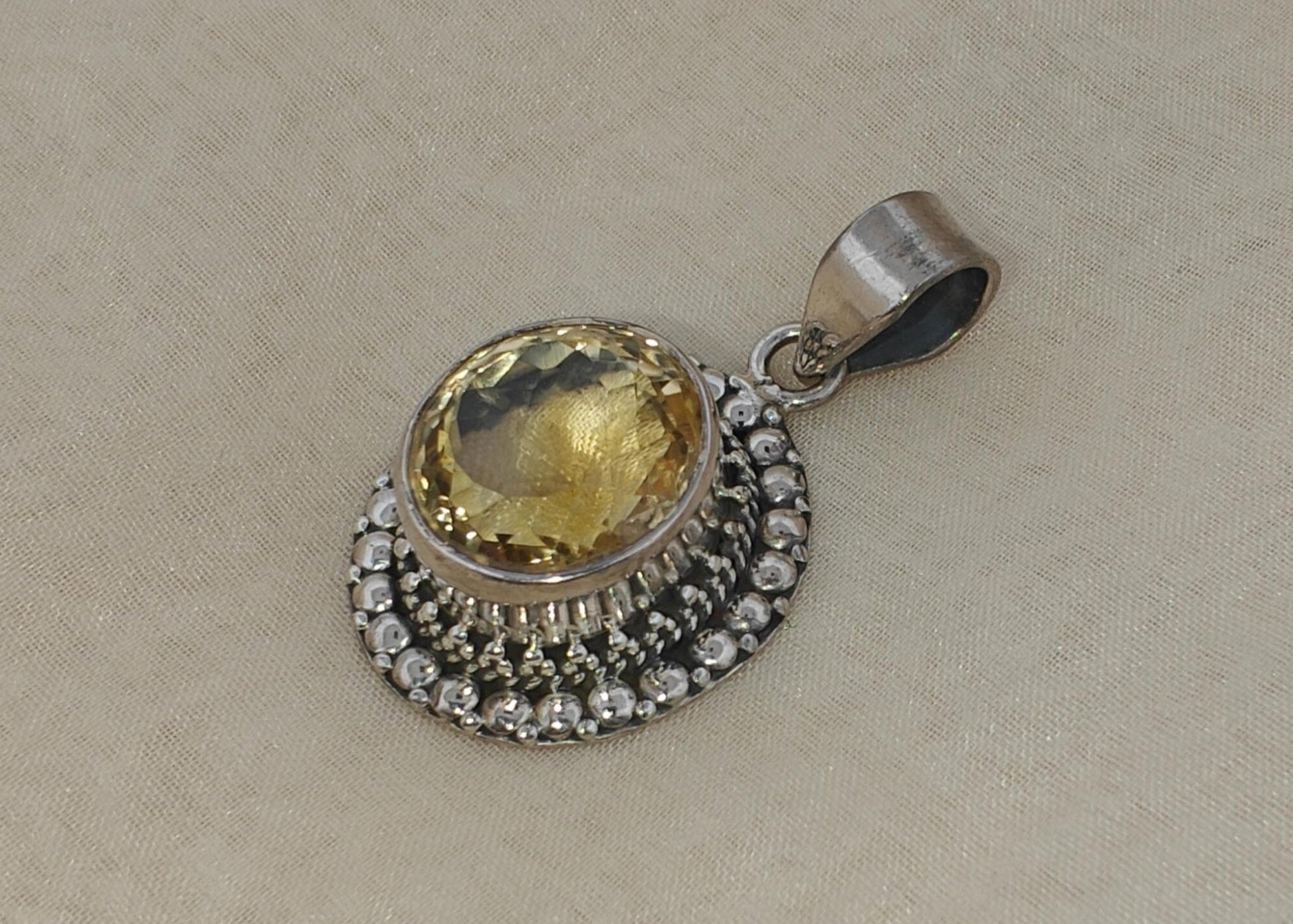 Silver pendant with a yellow gemstone on a beige fabric background