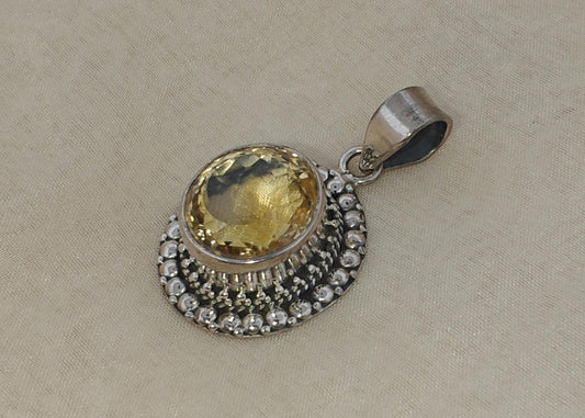 Silver pendant with a yellow gemstone on a beige fabric background