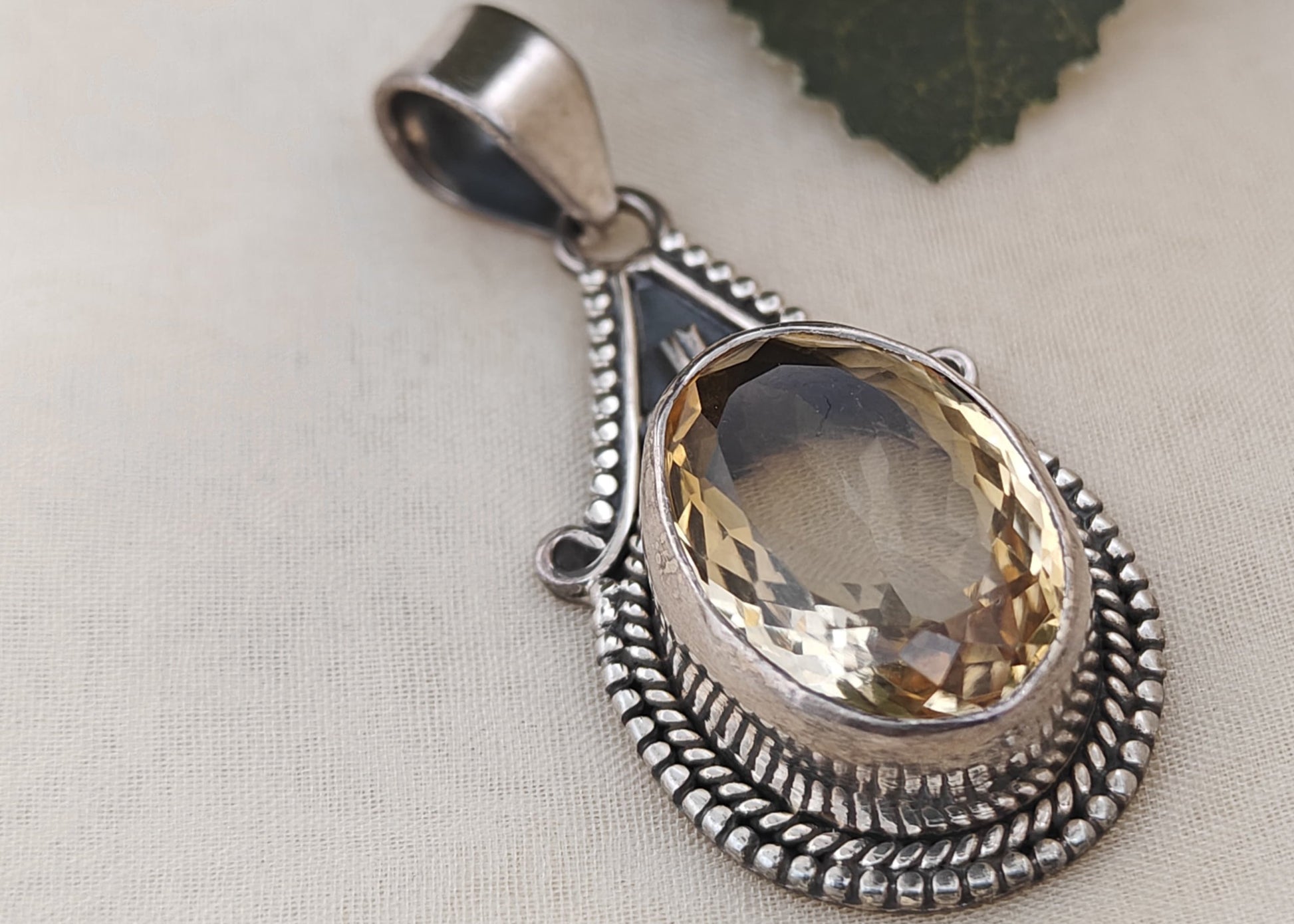 Silver pendant with a yellow gemstone on a light background