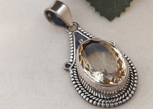 Silver pendant with a yellow gemstone on a light background