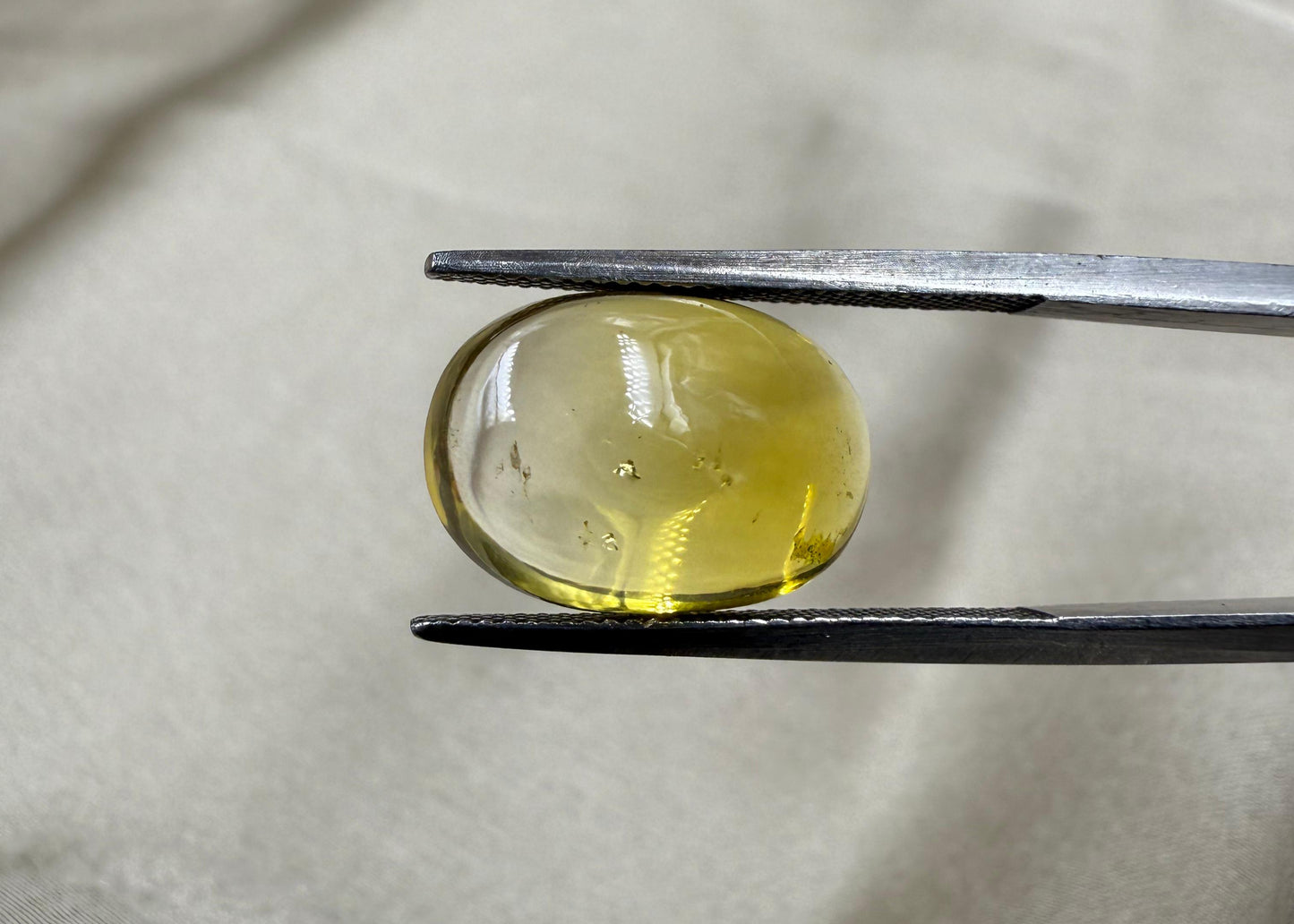 Clear gemstone held by tweezers on a light fabric background