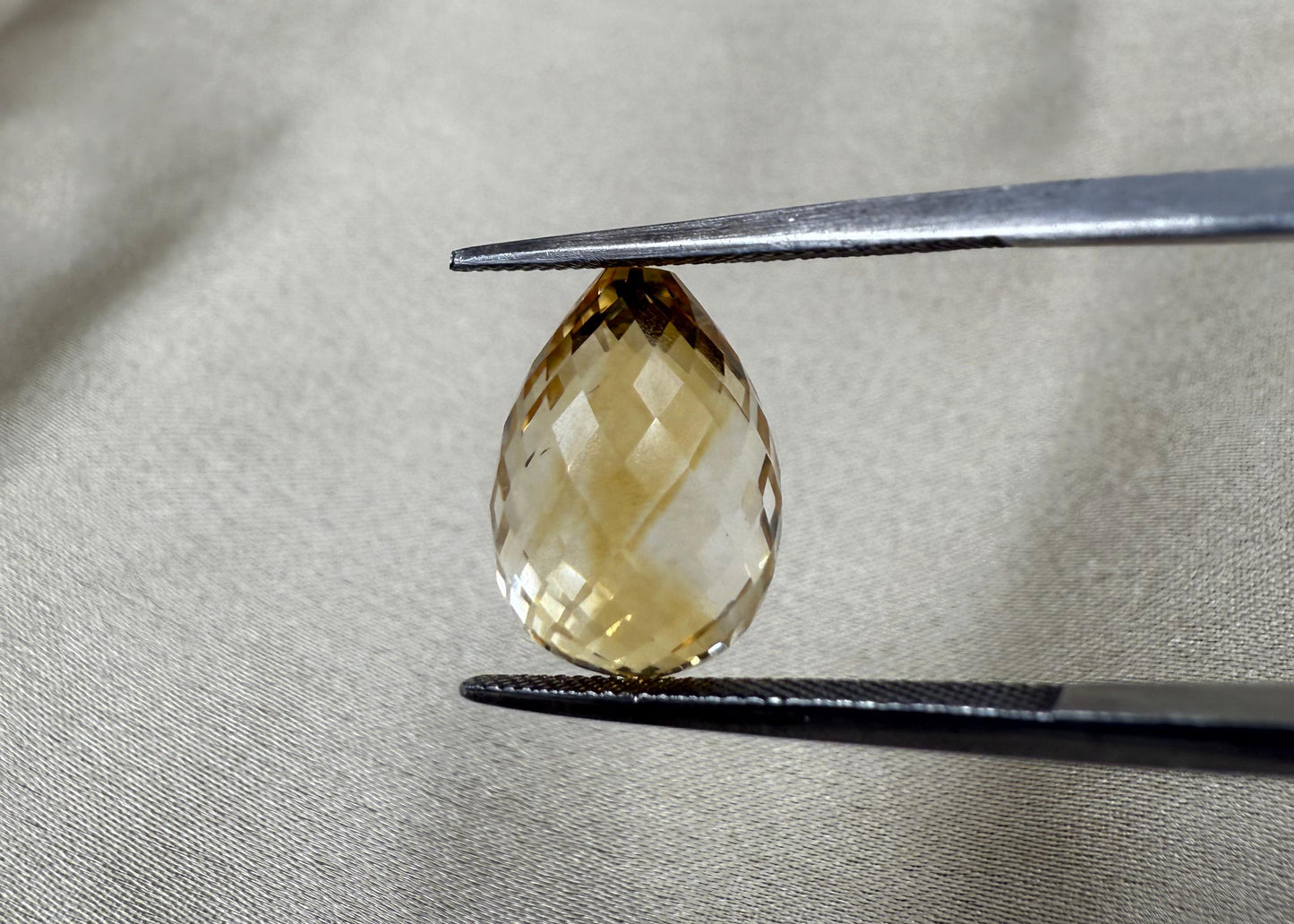 Faceted yellow gemstone held by tweezers on a gray fabric background