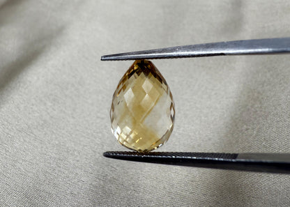 Faceted yellow gemstone held by tweezers on a gray fabric background
