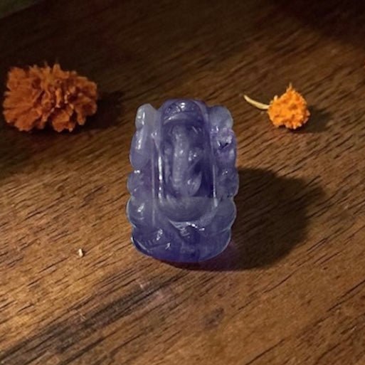 Natural dark amethyst Ganesh carved figure on wooden surface