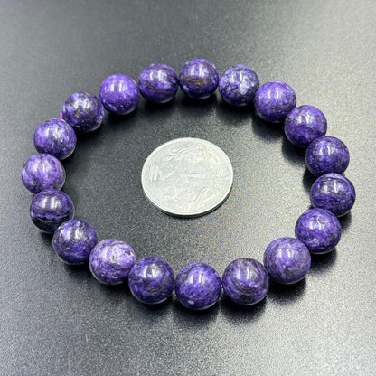 Charoite Bracelet with polished round purple beads arranged around a silver coin on black surface
