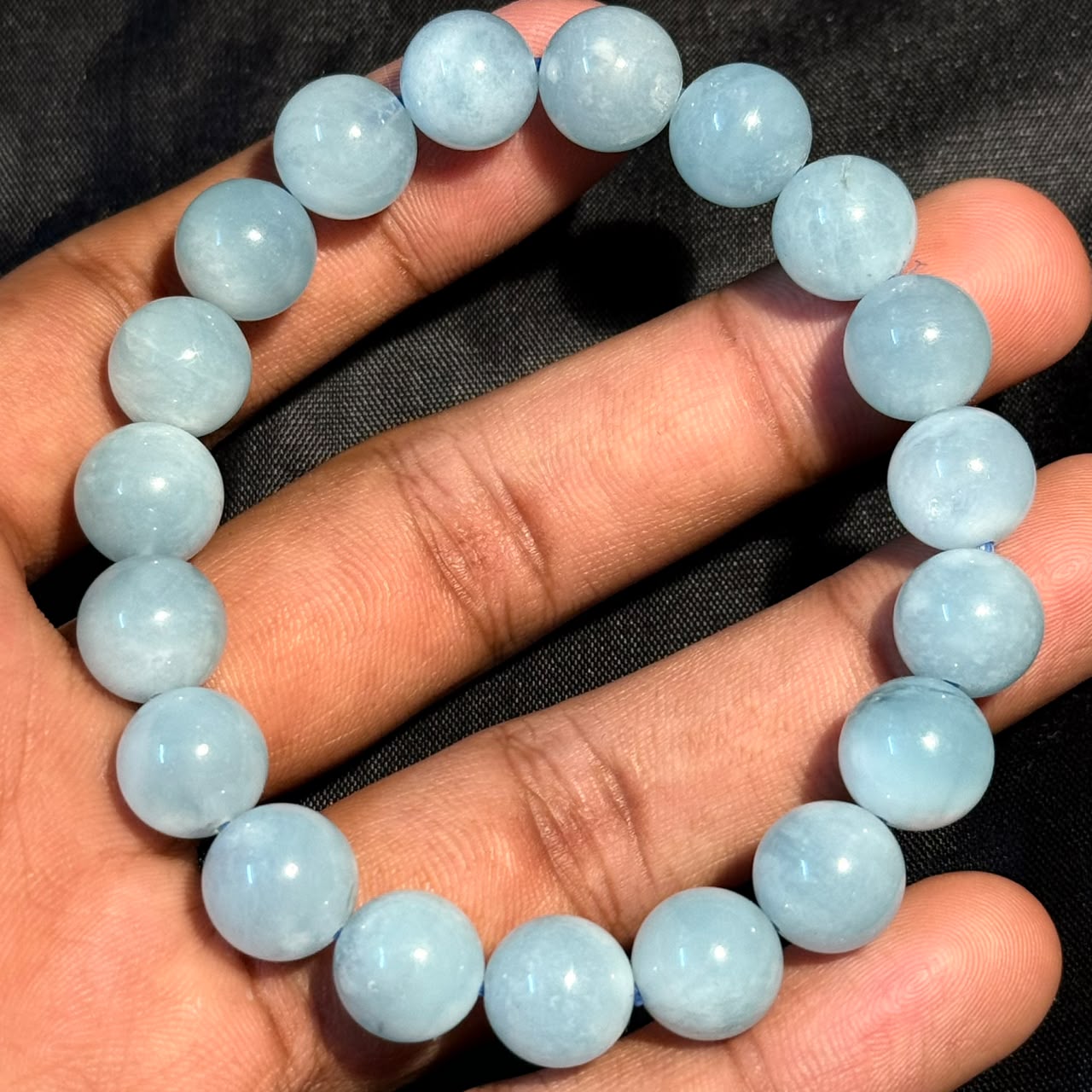 Aquamarine Bracelet held in hand showing round light blue polished beads on black background