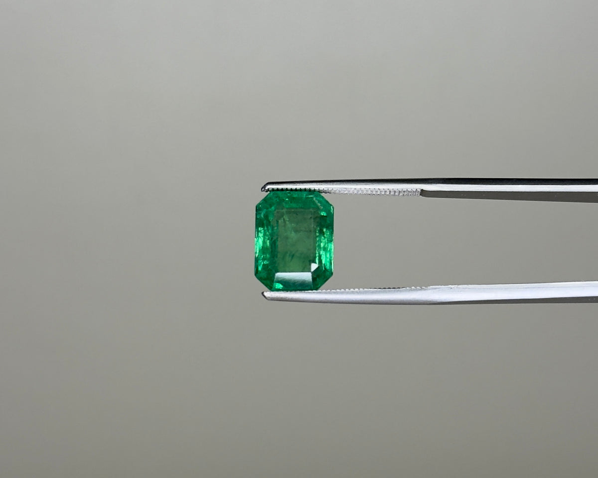 Emerald green gemstone in an emerald-cut setting held on tweezers