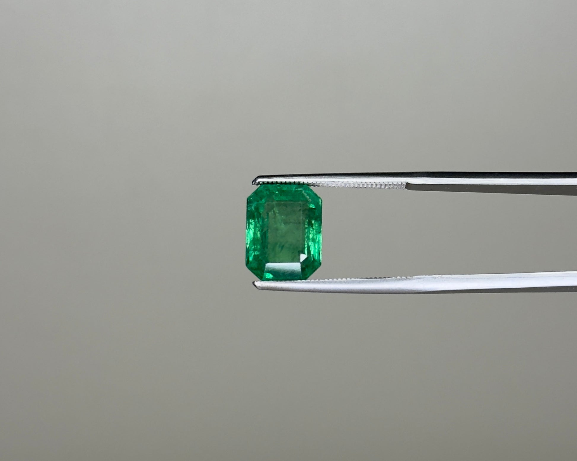 Emerald green gemstone in an emerald-cut setting held on tweezers