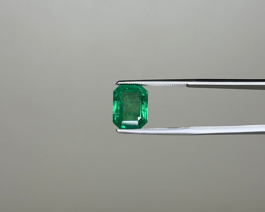 Emerald green gemstone in an emerald-cut setting held on tweezers