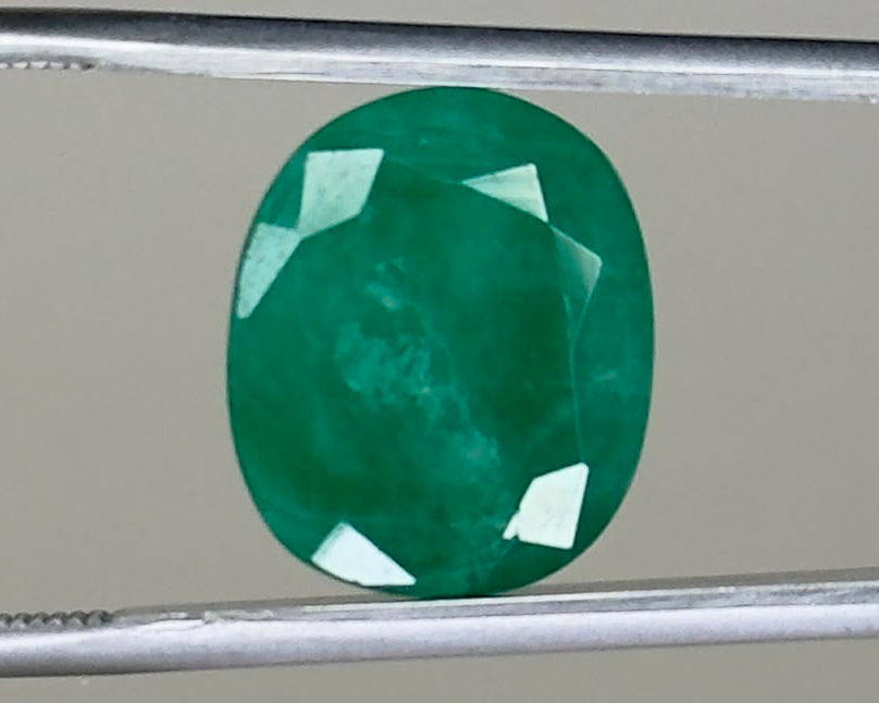 Emerald green oval gemstone with visible facets on a metal holder