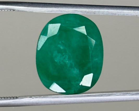 Emerald green oval gemstone with visible facets on a metal holder