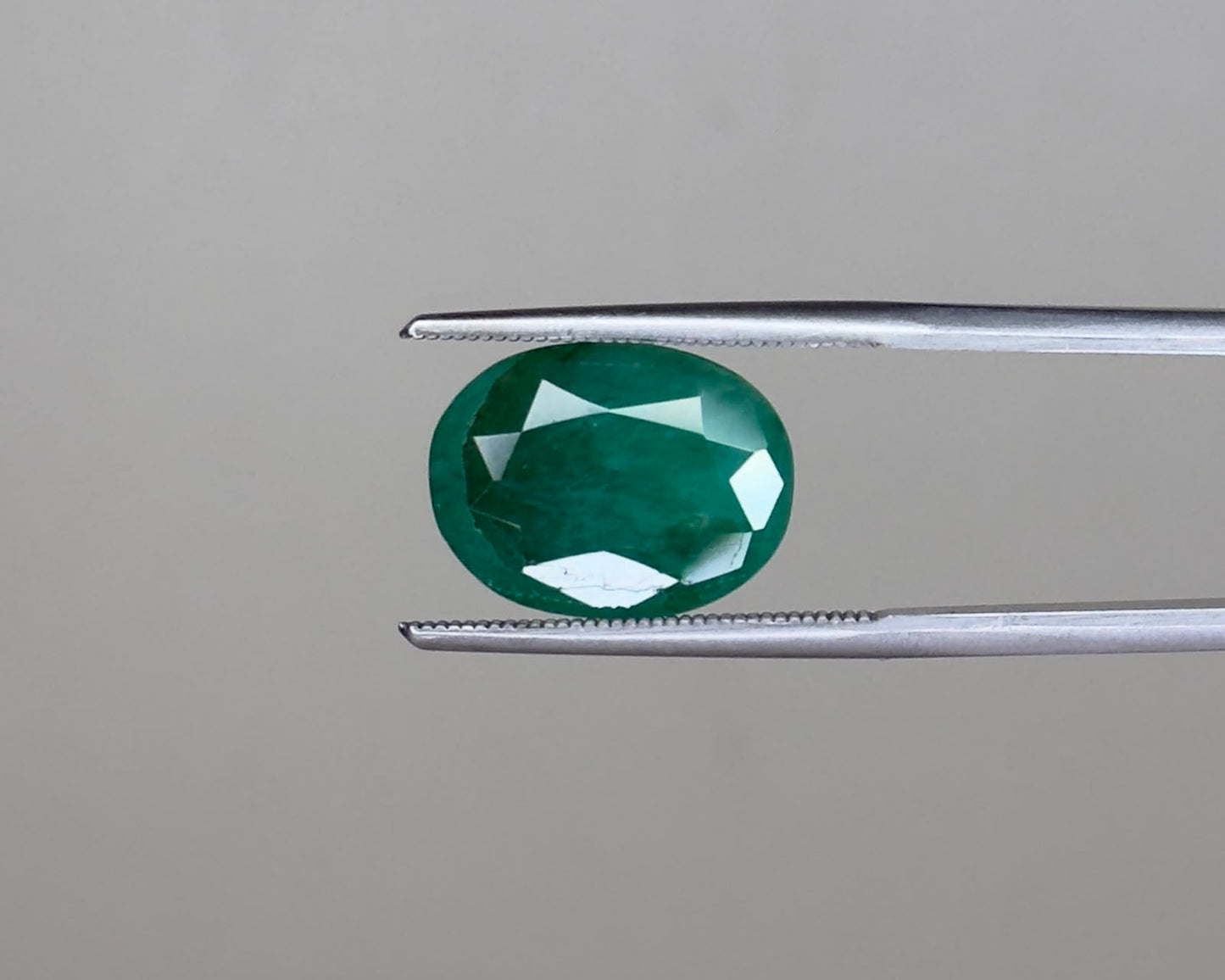 Emerald oval cut gemstone on tweezers with visible facets and deep green color
