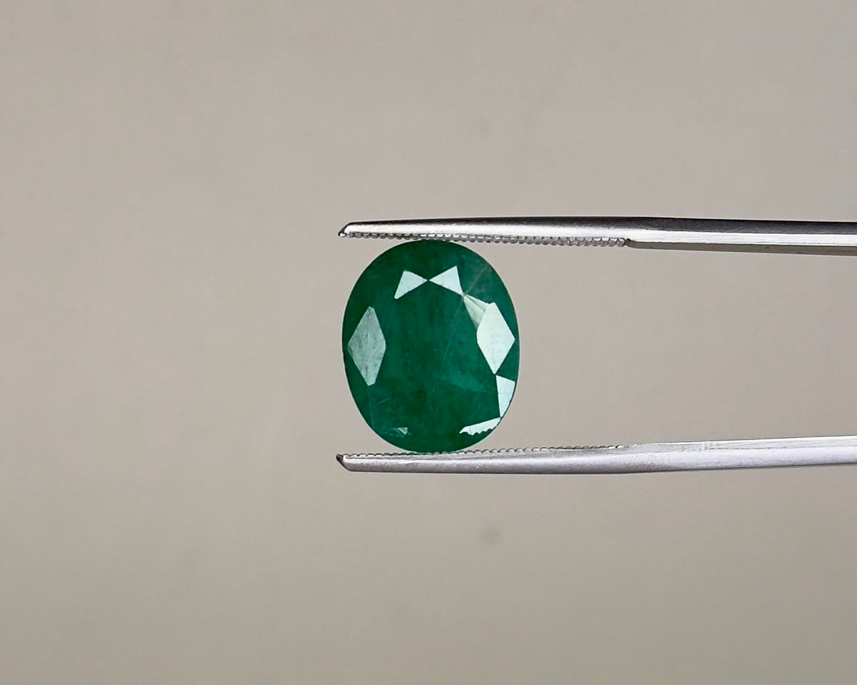 Emerald oval gemstone with faceted cut held between tweezers