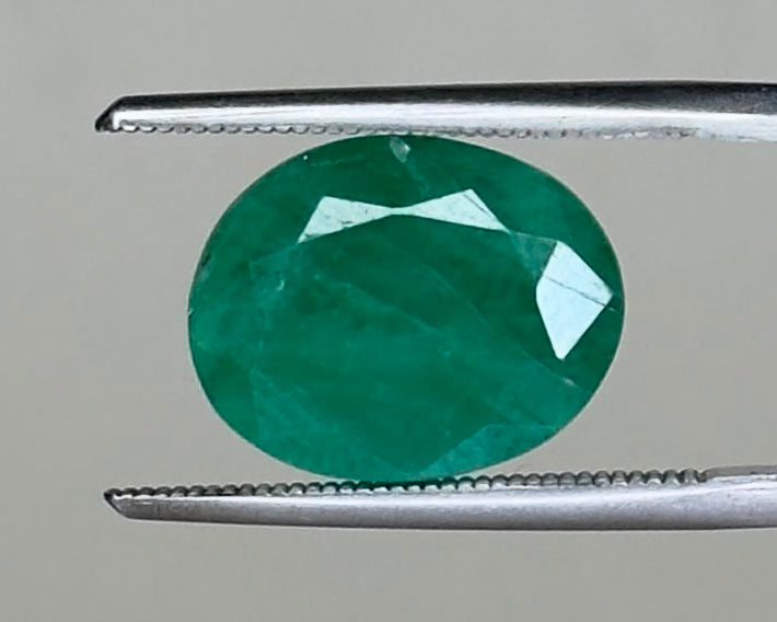 Emerald green round gemstone held with tweezers, faceted pavilion view