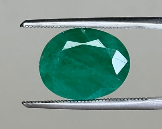 Emerald green round gemstone held with tweezers, faceted pavilion view