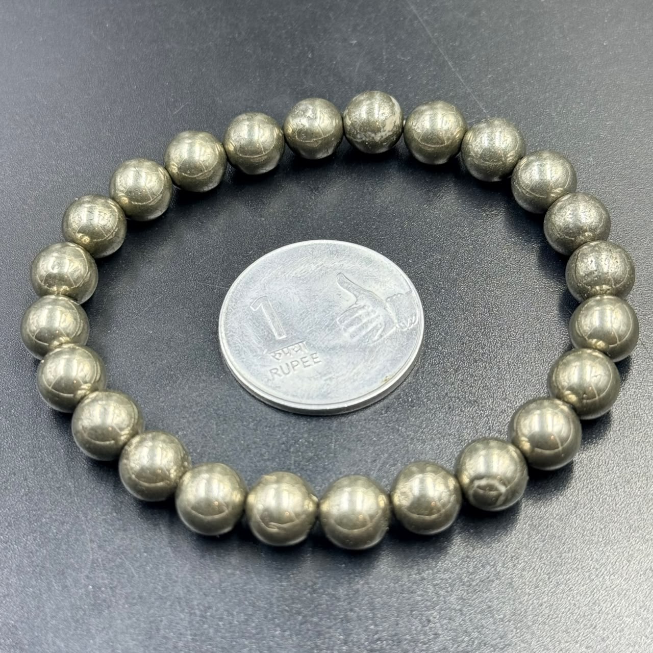 Pyrite Bracelet (Wealth and Confidence) with round metallic beads next to a one rupee coin on black surface