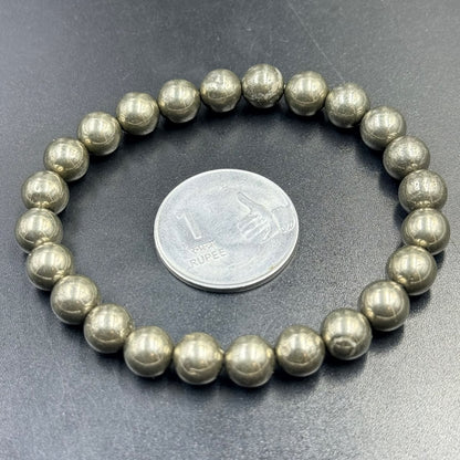 Pyrite Bracelet (Wealth and Confidence) with round metallic beads next to a one rupee coin on black surface
