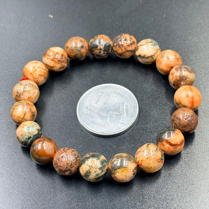 Beaded fire agate bracelet with round orange and green stones beside a coin for scale