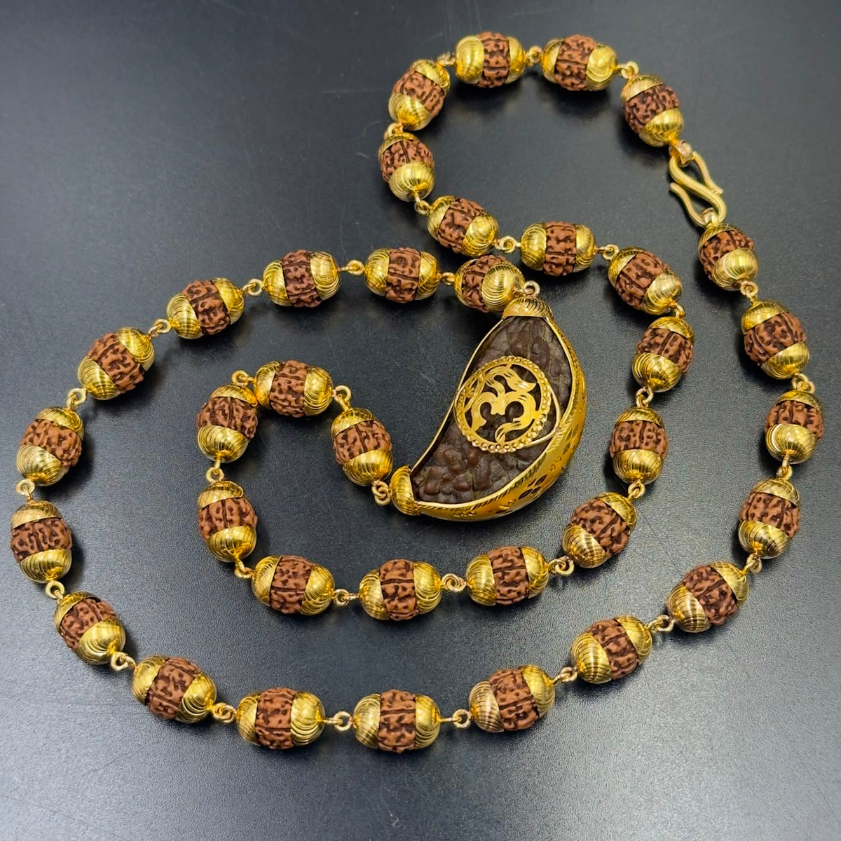 Gold-plated 925 silver rudraksha mala with Om pendant centerpiece on dark slate