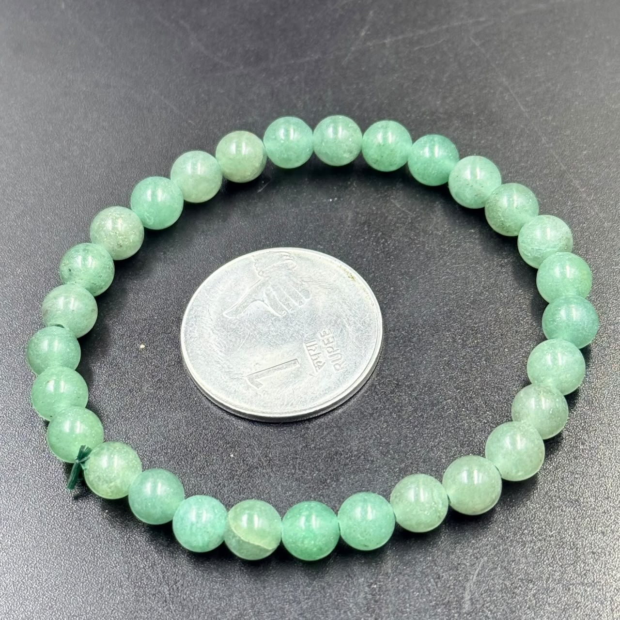 Round green aventurine bead bracelet on dark surface with coin for size