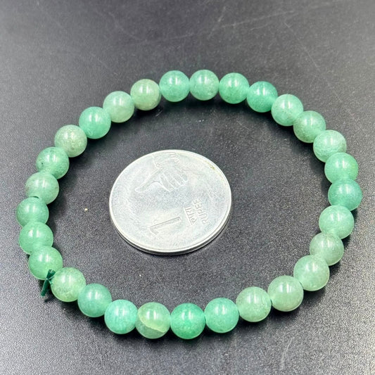 Round green aventurine bead bracelet on dark surface with coin for size