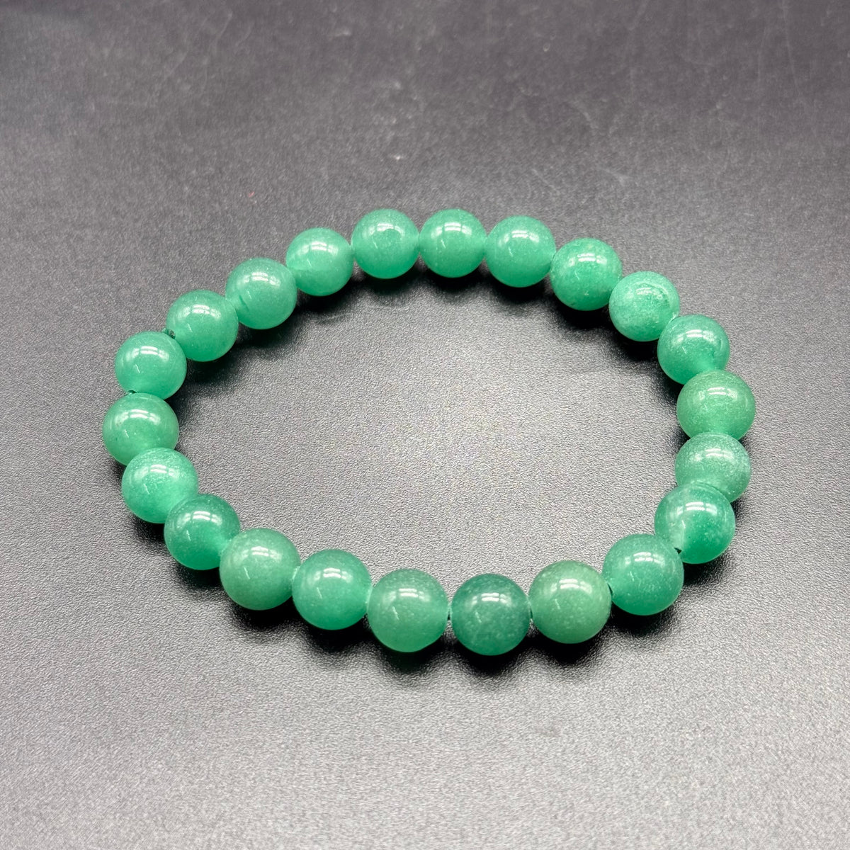 Green aventurine beaded bracelet with glossy round stones on gray background