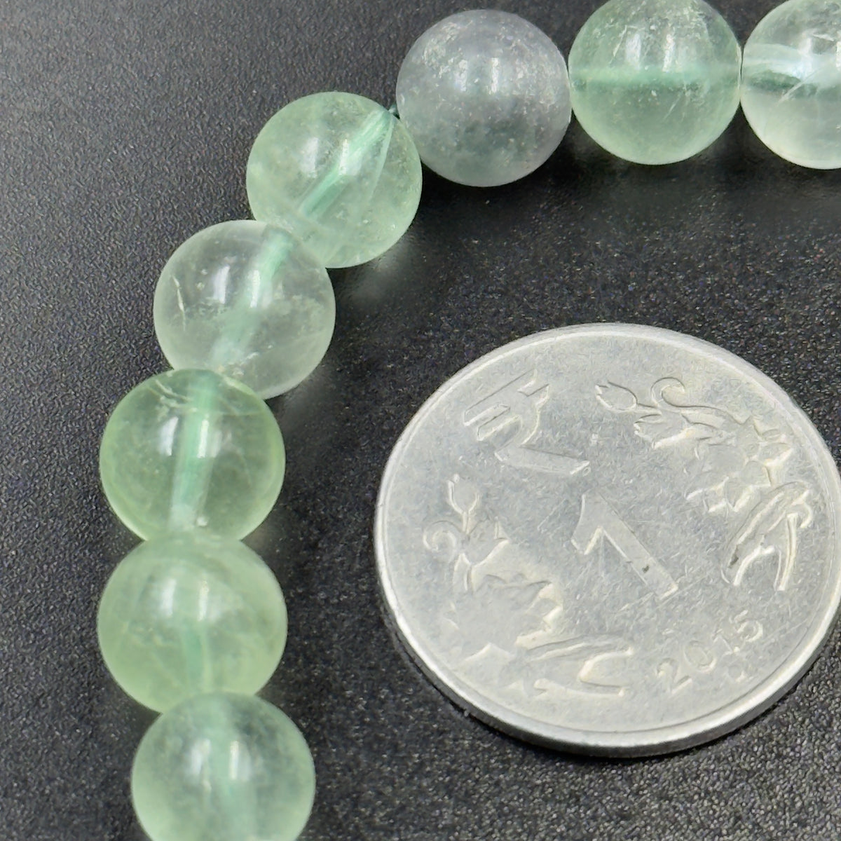 Macro view of green fluorite bracelet beads next to a coin for scale