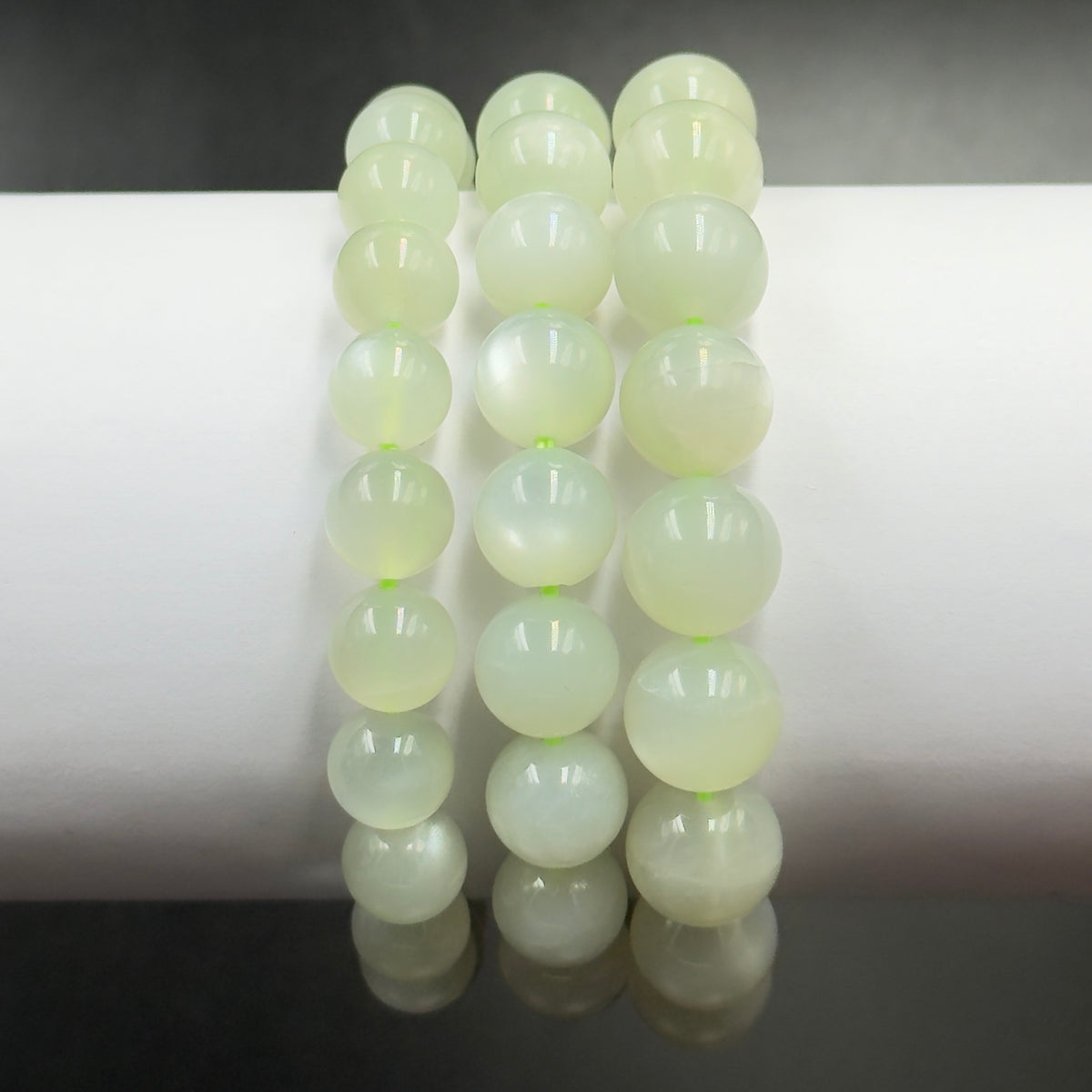 Close-up of green moonstone bracelet round beads reflecting light against a white background