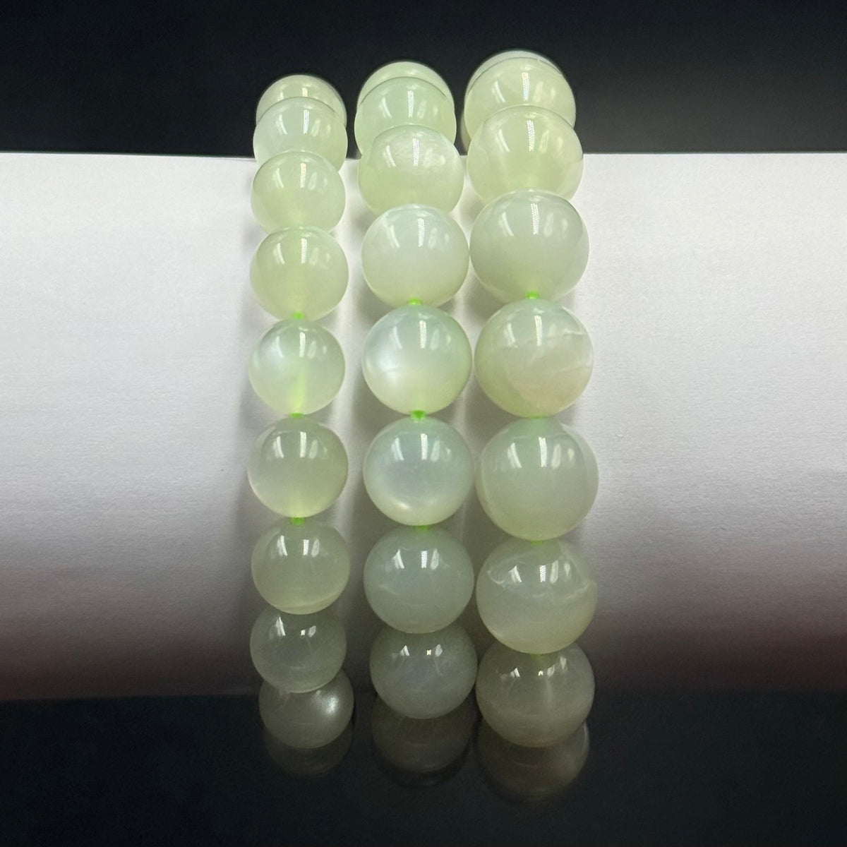 Close-up of green moonstone bracelet beads reflected on a dark tabletop with bright white background