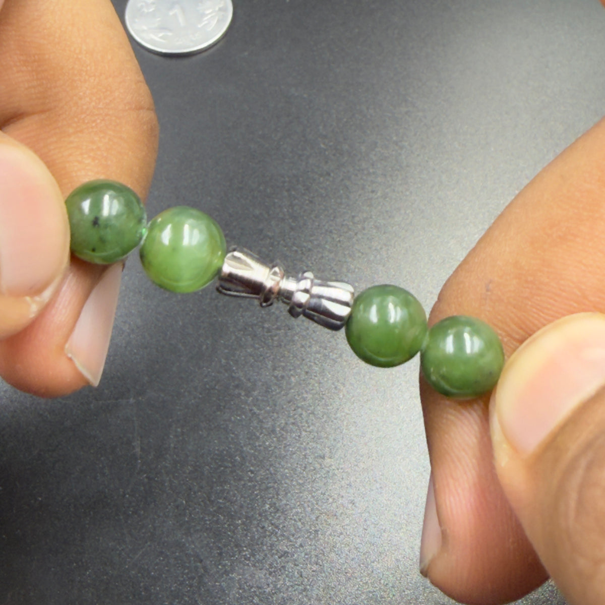 Close-up of natural green nephrite jade beads with silver clasp held in hands
