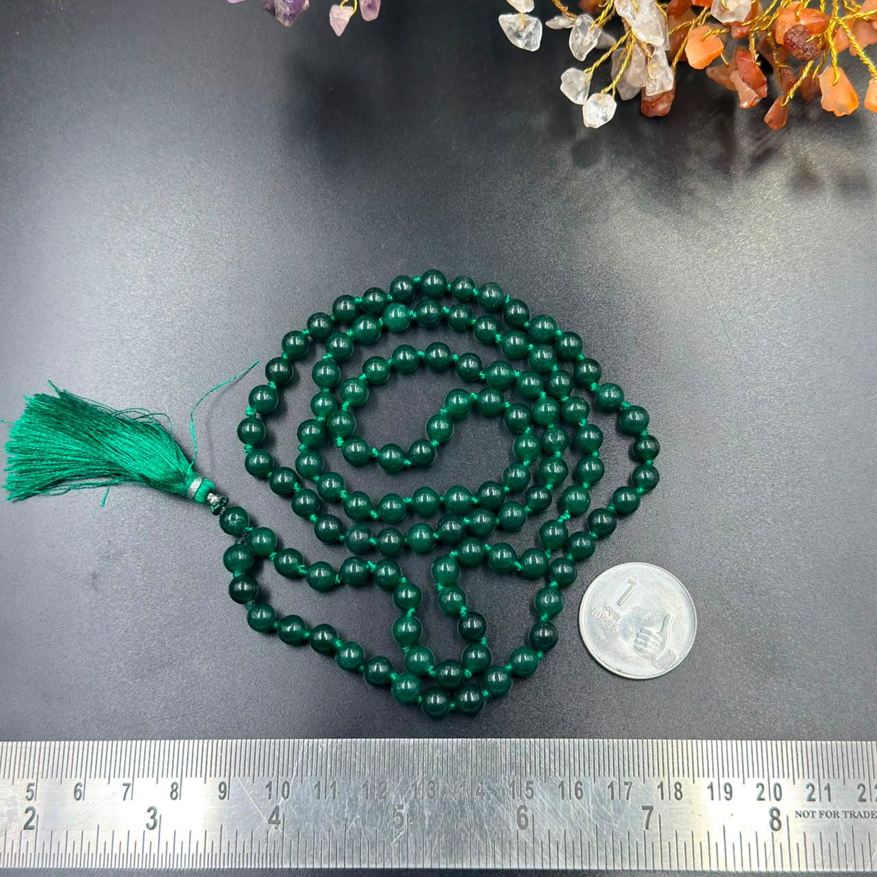 Green onyx jaap mala beads with tassel and ruler for size, spread on a dark surface