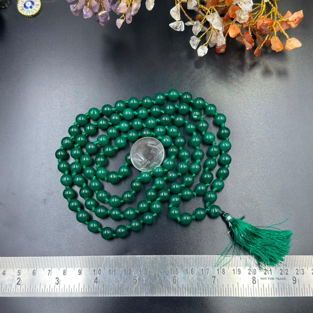 Green onyx jaap mala necklace strands with tassel and coin for scale on dark surface