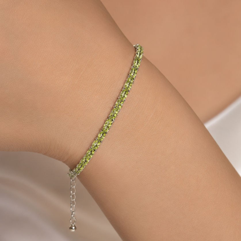 Green peridot tennis bracelet on wrist with silver chain and dangling clasp