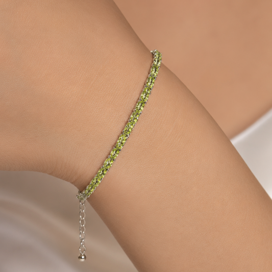 Green peridot tennis bracelet on wrist with silver chain and dangling clasp