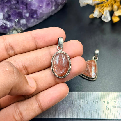 Sunstone silver locket pendant in an oval frame held in hand, with textured border