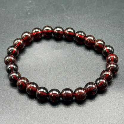Hessonite Garnet (Gomed) bracelet with 8mm polished round beads in deep reddish-brown on gray background