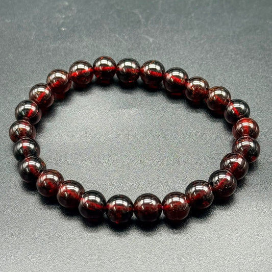 Hessonite Garnet (Gomed) bracelet with 8mm polished round beads in deep reddish-brown on gray background