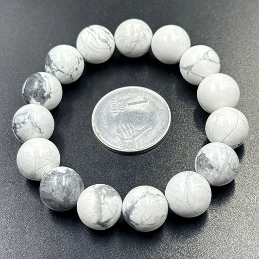 Close-up of white howlite round beads bracelet with coin for scale on dark background