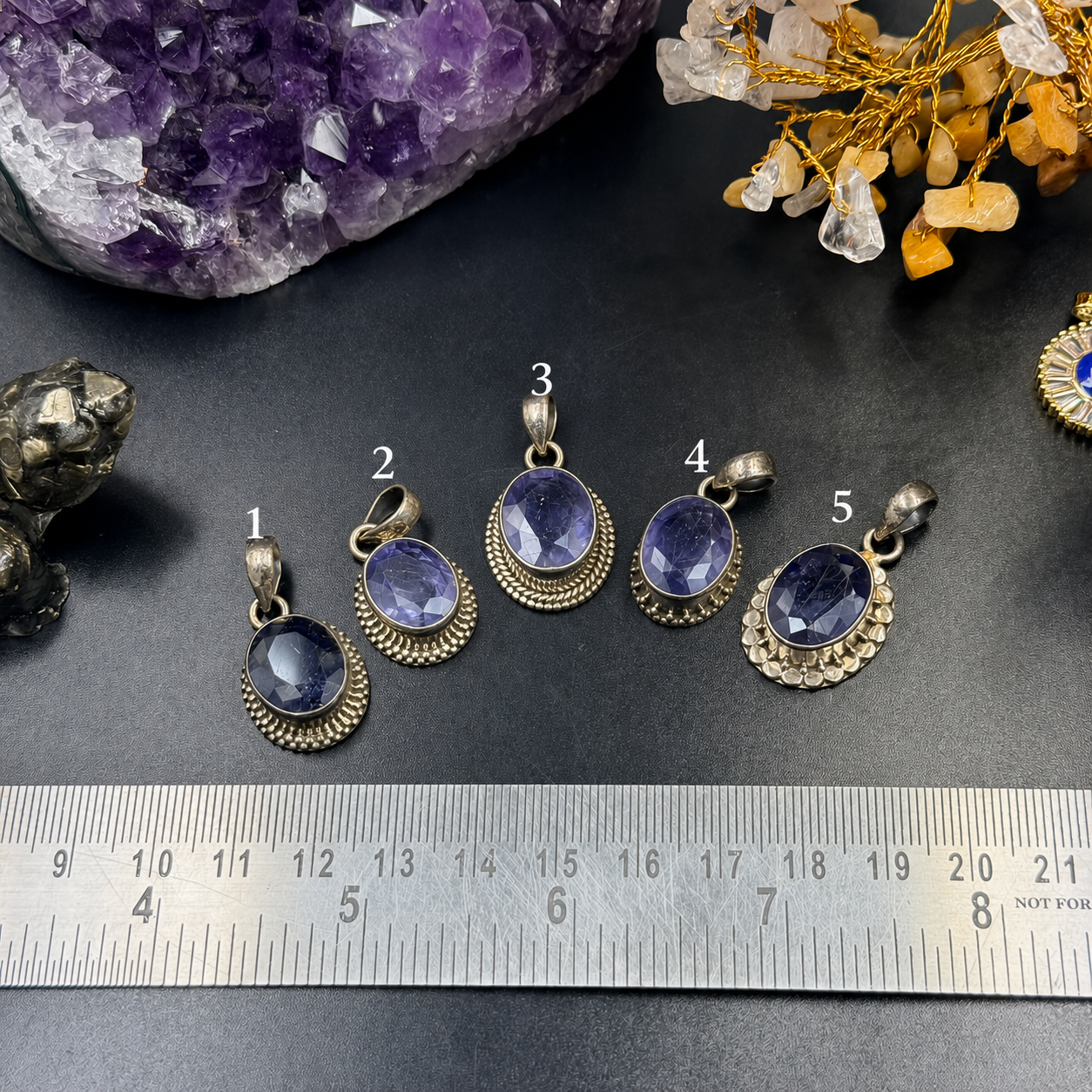 Five iolite 925 silver locket pendants with textured oval bezels on measuring ruler