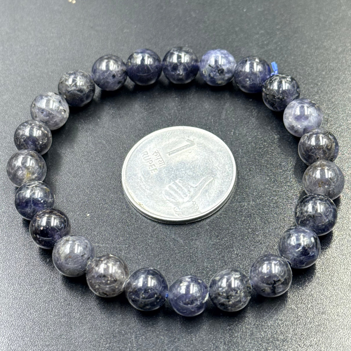 Close-up of iolite bead bracelet with beads and coin for scale on gray background