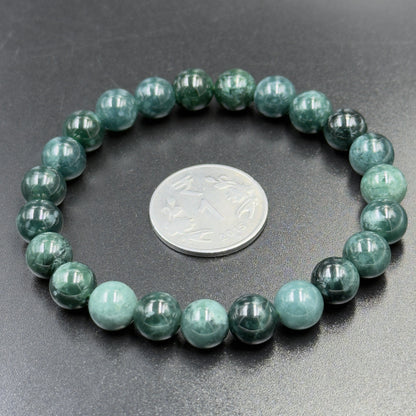 Close-up of jadeite jade AAA bead bracelet with coin for size on dark gray background