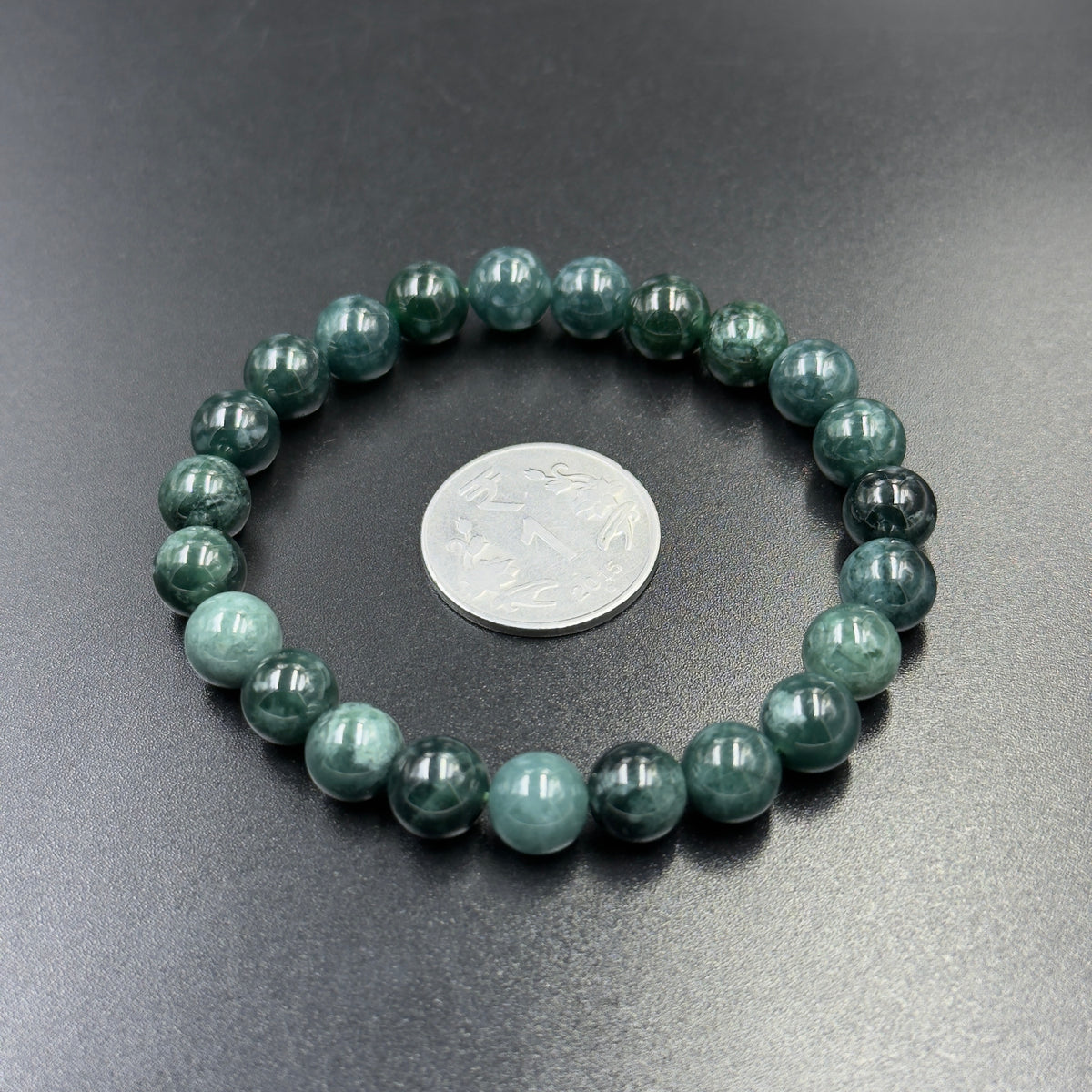 Jadeite jade AAA bead bracelet close-up with coin for scale on dark gray background