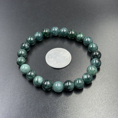 Jadeite jade AAA bead bracelet close-up with coin for scale on dark gray background