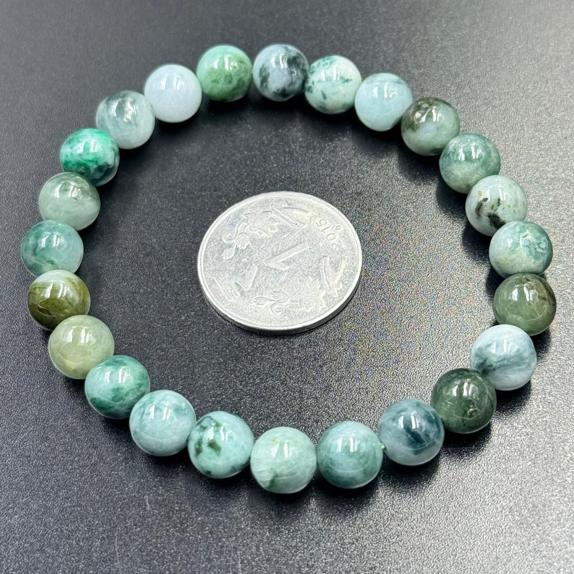 Jadeite jade bracelet close-up of round apple green and lavender beads on dark gray background