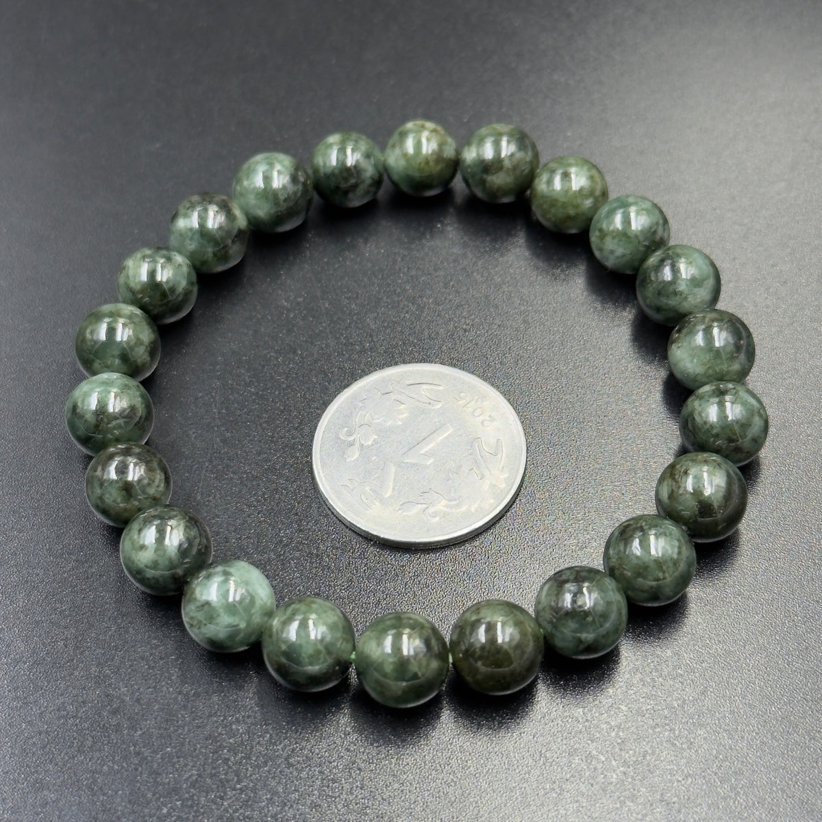 Round jadeite jade bracelet beads with coin for scale on dark textured background