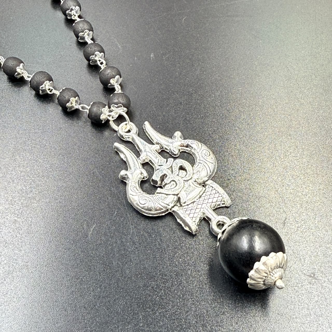 Karungali bead mala with Om Trishul metal pendant and silver clasp on grey background